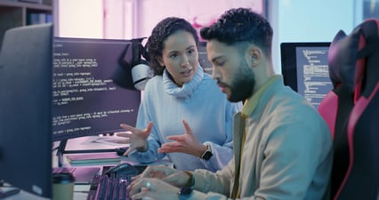 Male and female IT employees discussing updates in cyber security strategies at their workstations